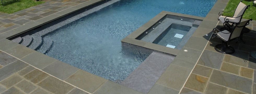 A pool with a stone deck and water feature.